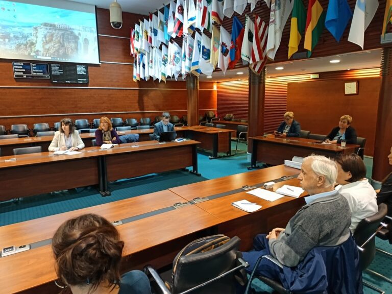 Felzárkózási Fórum ülés nagy tanácsteremben, U-asztalos elrendezésben ülő résztvevőkkel, a falon zászlók és hivatalos jelképek láthatók.