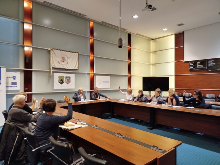 Szavazás a Felzárkózási Fórum Munkacsoport ülésén, résztvevők kézfeltartással döntenek egy napirendi kérdésről.