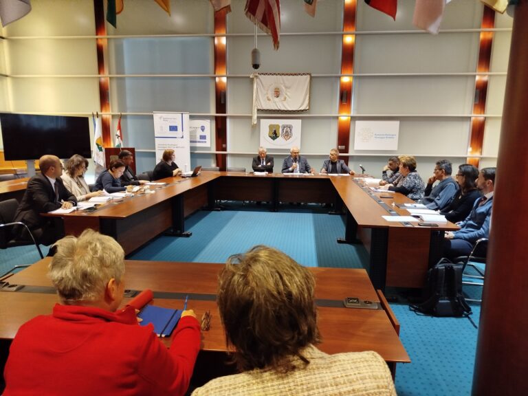 Felzárkózási Fórum ülés nagy tanácsteremben, középen az elnöklő asztal, háttérben hivatalos jelképek és zászlók.